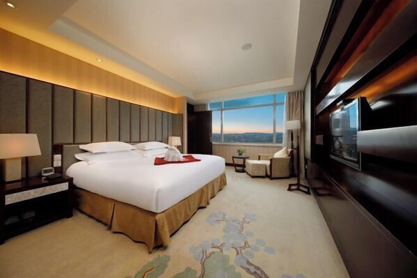 Habitación de hotel con una cama grande, mesitas de noche, televisor y vistas a la ciudad.