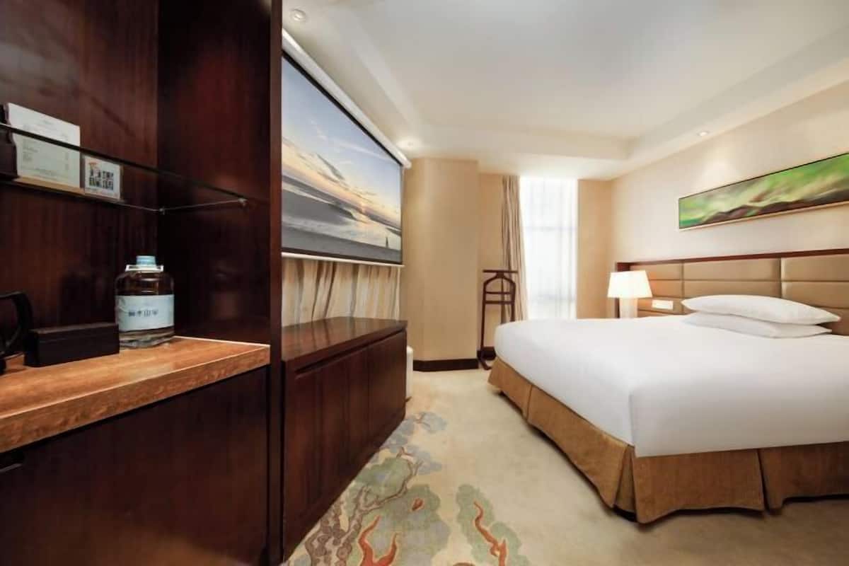 A hotel room with a bed, a desk, a chair, a TV, and a painting on the wall.