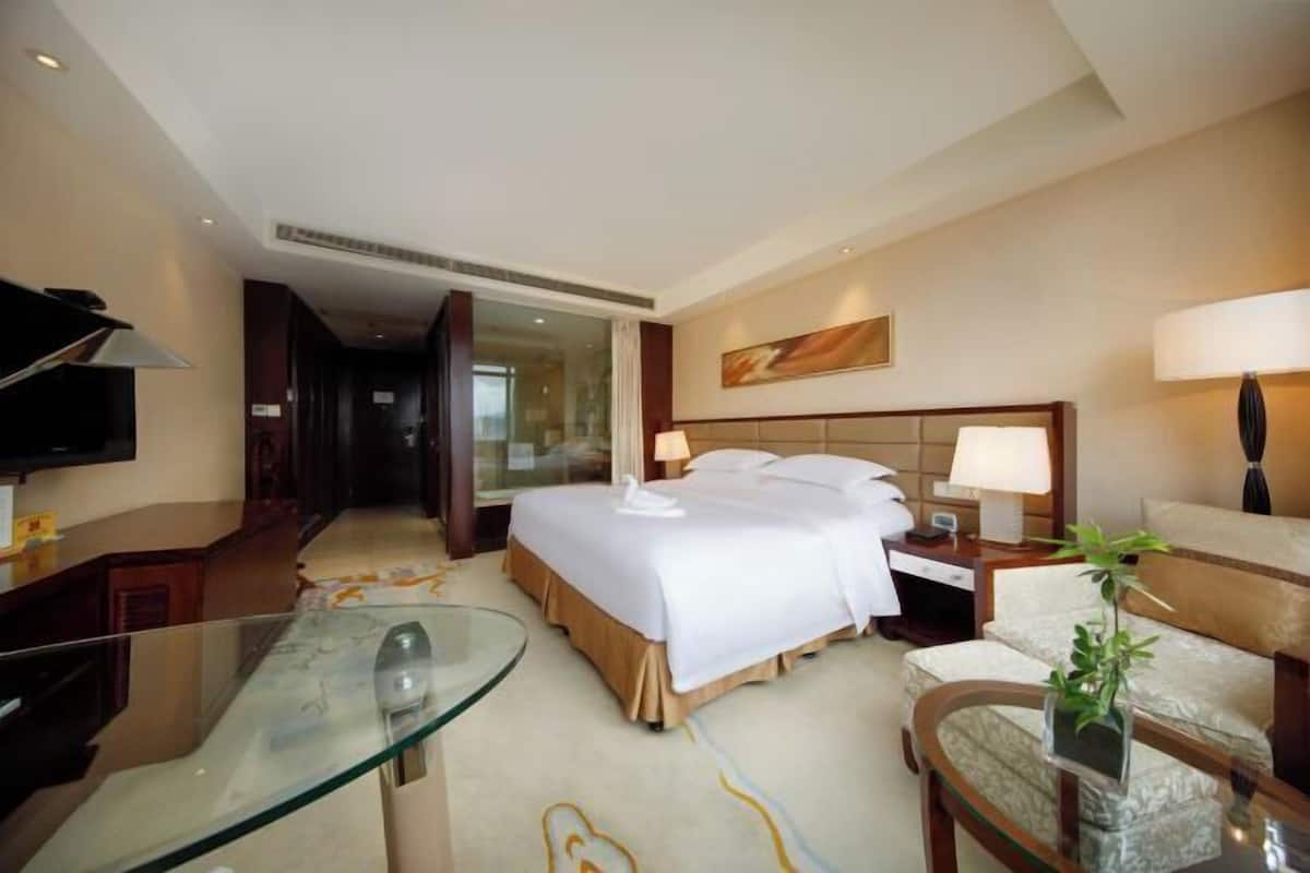 A hotel room with a bed, bedside tables, a glass table, a sofa, and a TV.