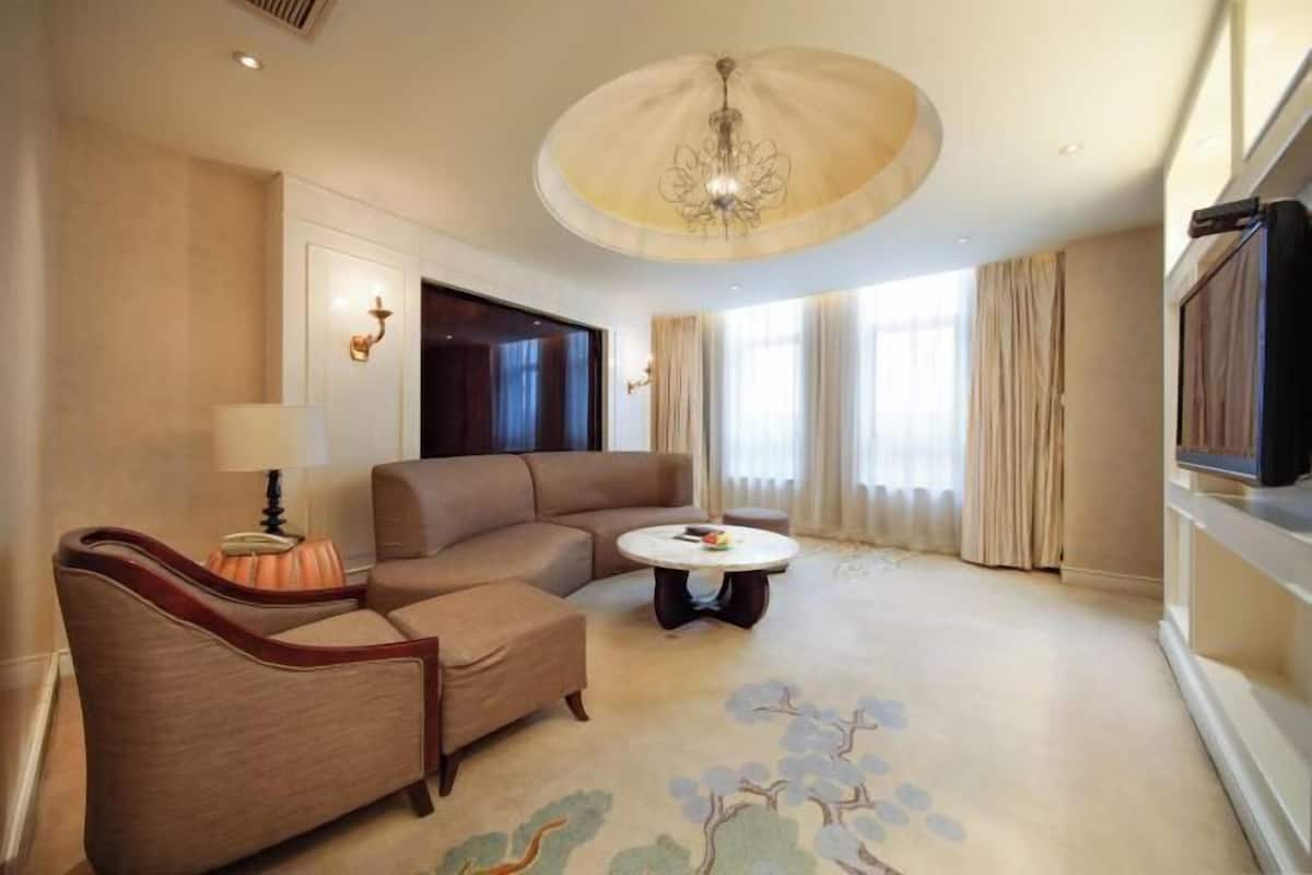 A hotel room with a large sofa, a small armchair, a round coffee table, and a television.