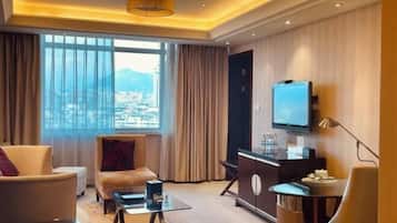 A modern hotel room with a large window, a flat-screen TV, a desk, and a sofa.