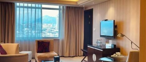 A modern hotel room with a large window, a flat-screen TV, a desk, and a sofa.