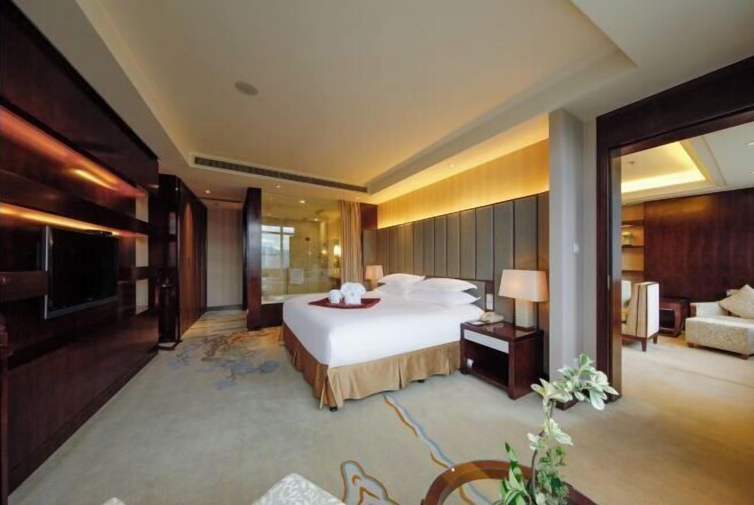 A hotel room with a large bed, bedside tables, a television, and a view of the hallway.
