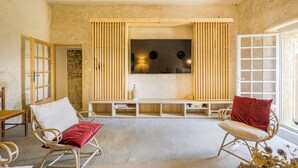 A spacious living area with a large flat-screen TV, wooden furniture, and a stone wall. - Domaine Clément Sainte Victoire, 7ha of tranquility 17 km from Aix (Puyloubier)