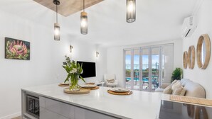 A modern kitchen with a large island, pendant lighting, a flat-screen TV, and a view of the outdoors.