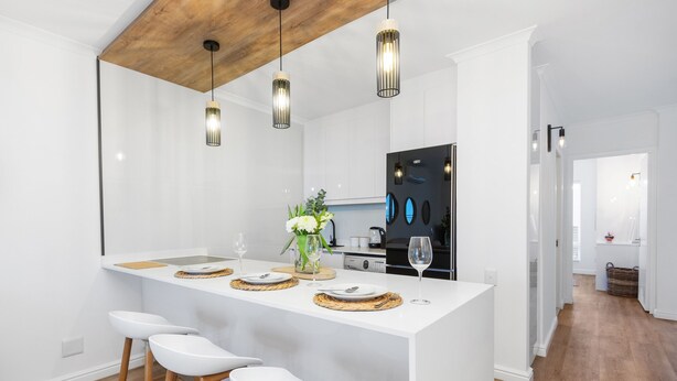 A modern kitchen with white cabinetry, a central island with bar stools, pendant lighting, and a refrigerator.