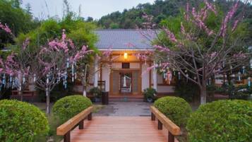 A traditional building with a wooden entrance, surrounded by well-maintained greenery and a wooden pathway leading to it.
