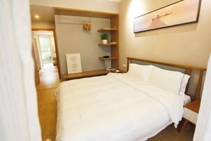 Un dormitorio con una cama, una mesita de noche, un estante con una planta y un cuadro enmarcado.