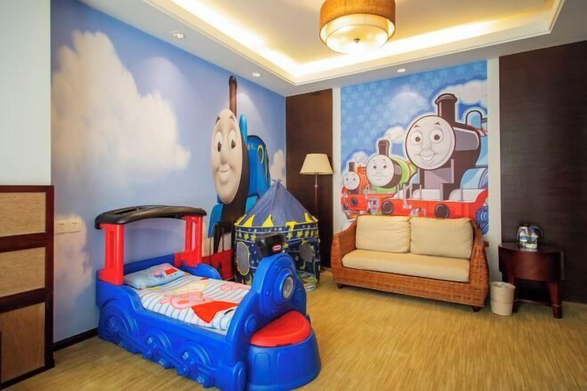 A children's room with a bed, a sofa, and a wall mural of Thomas the Train.