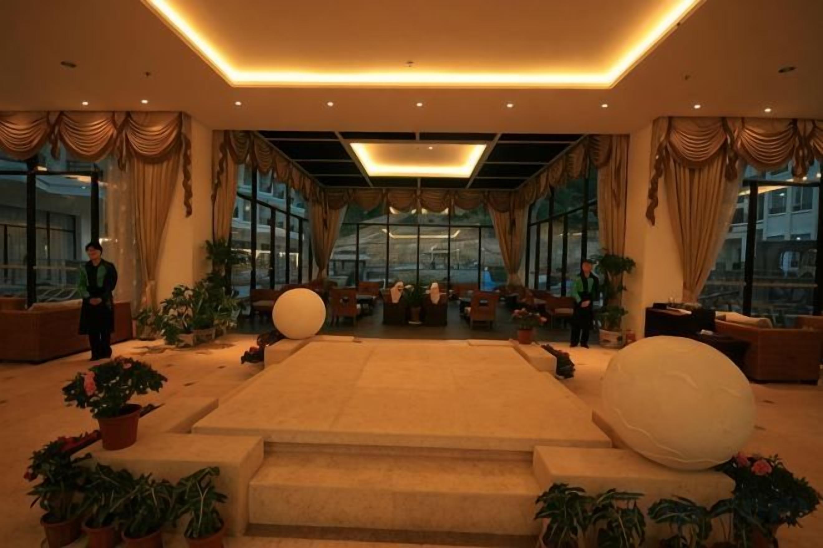 A spacious lobby with a central seating area, large windows, and potted plants.