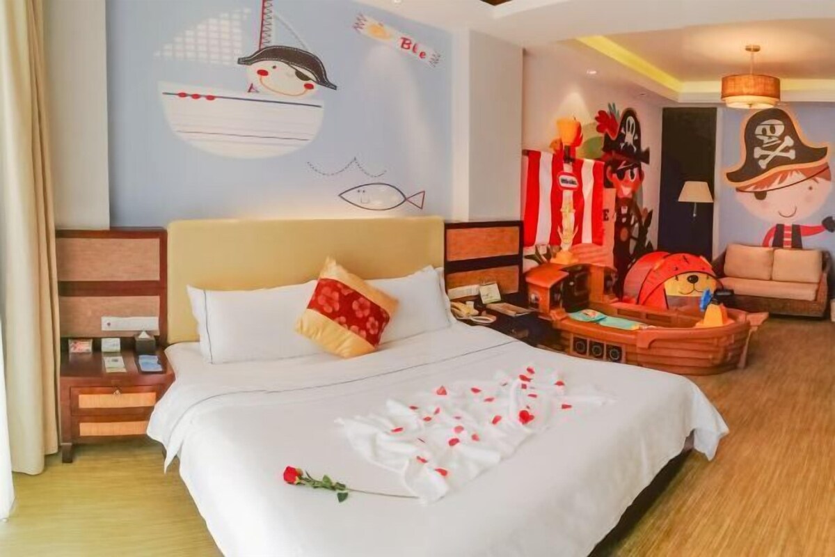 A hotel room with a bed, a nightstand, a small table, a decorative wall with a pirate theme, and a cozy seating area with a chair and a small table.