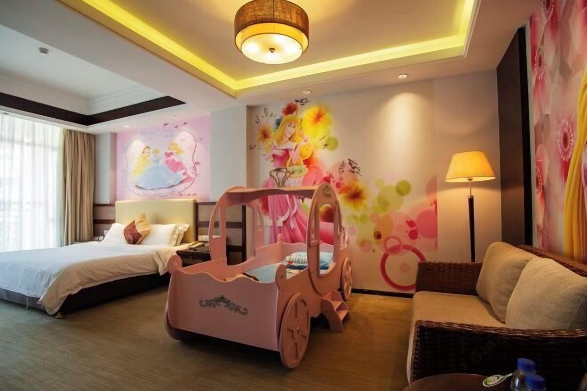 A hotel room with a bed, a pink toy car, a sofa, and a lamp.
