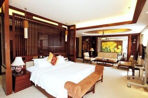 A hotel room with a large bed, a sitting area with a sofa and chairs, a desk, and a painting of flowers. - Xihai Hot Spring Holiday Hotel (Yongxiu)