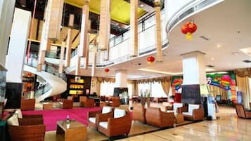 A spacious lobby with a curved staircase, comfortable seating areas, and a large digital screen.