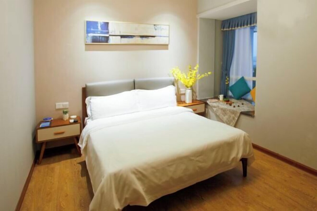 A neatly arranged hotel room with a bed, bedside table, and a small table with a vase of flowers.