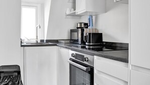 Une cuisine compacte avec des meubles blancs, un plan de travail noir, un four à micro-ondes, une machine à café et un four.