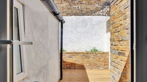 Une étroite terrasse en bois mène à un mur de briques sur lequel se trouve une fenêtre, à gauche.