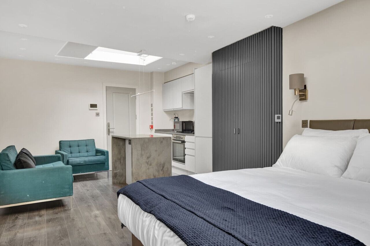 Ein modernes Hotelzimmer mit einem großen Bett, einer Sitzecke, einer Küchenzeile und Blick auf die Stadt.