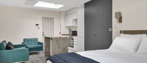 Ein modernes Hotelzimmer mit einem großen Bett, einer Sitzecke, einer Küchenzeile und Blick auf die Stadt.