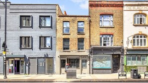 Une rangée d’immeubles à étages, avec différentes boutiques en façade, dont une entrée bien visible menant à un commerce.