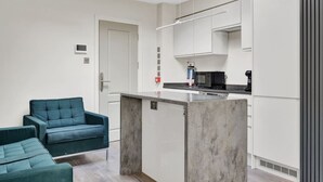 Une cuisine moderne avec des meubles blancs, un micro-ondes noir et une machine à café. On y trouve un canapé de couleur turquoise et un îlot central en béton.