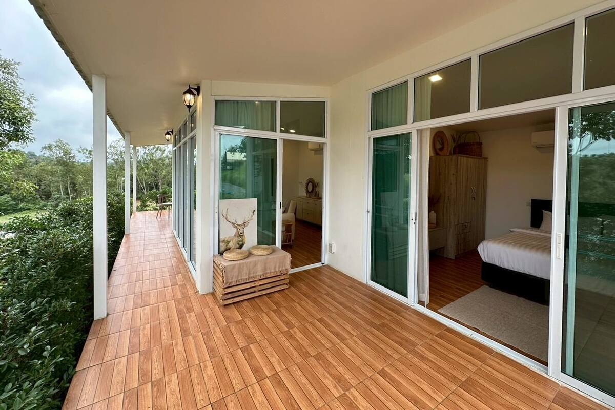 Une chambre moderne dotée d’une grande porte-fenêtre coulissante donnant sur un balcon. La chambre a un plancher en bois et un lit avec une tête de lit blanche.
