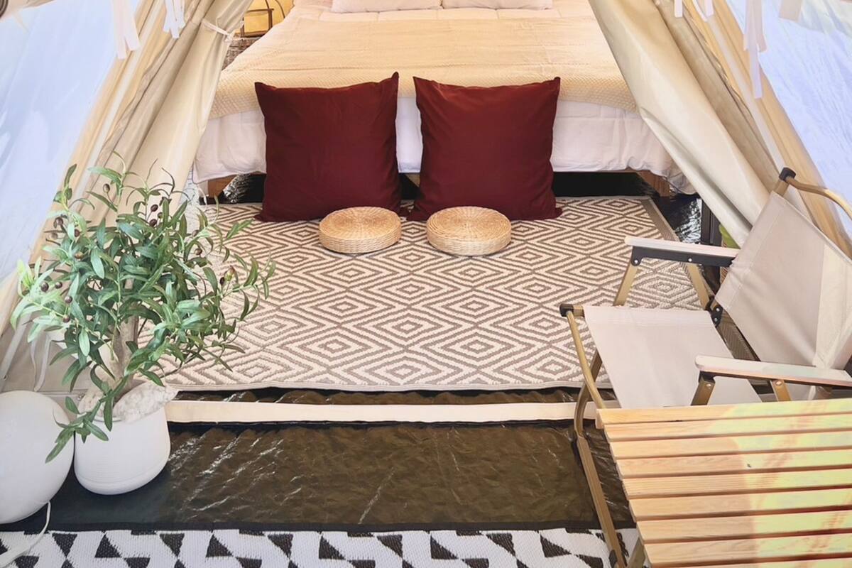 Une tente équipée d’un lit, d’oreillers, d’une petite table, d’une chaise et d’une plante.