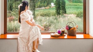 Une personne assise près d’une grande fenêtre, d’où l’on peut admirer un paysage verdoyant.