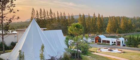 A tented accommodation with a paved driveway, a small building with a red door, and a view of a forested area.