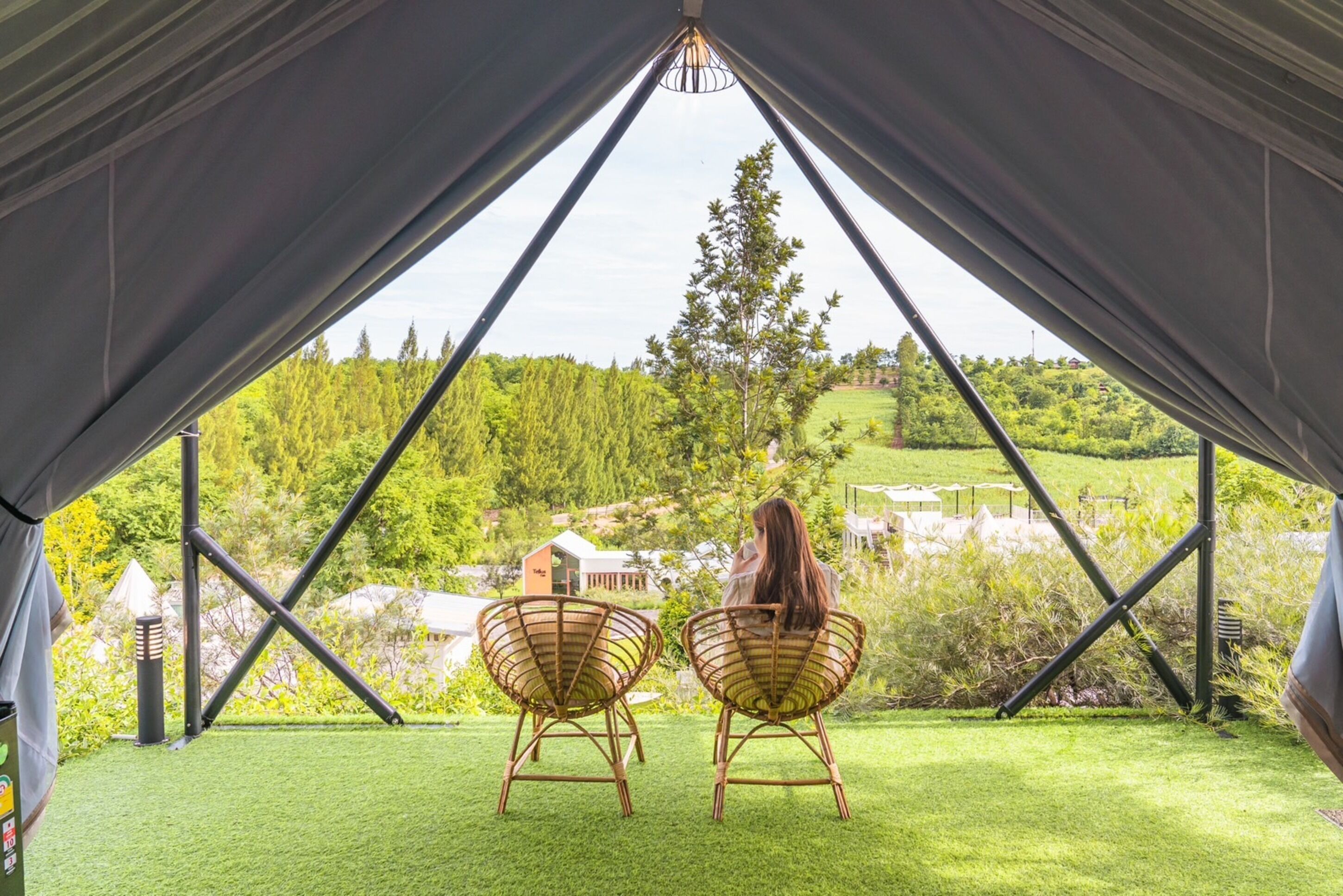 A tent with two wicker chairs facing a view of a green landscape and buildings.