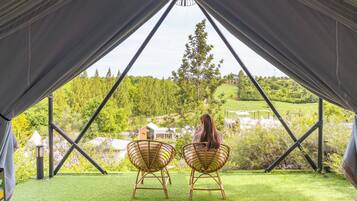 A tent with two wicker chairs facing a view of a green landscape and buildings.