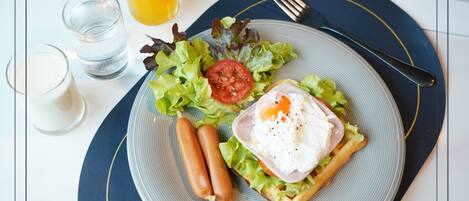 Un plato con un gofre, un huevo, lechuga y tomates, acompañado de un vaso de zumo de naranja y un vaso de agua.