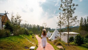 Un chemin mène à un bâtiment blanc doté d’un toit triangulaire, entouré de verdure et d’arbres.