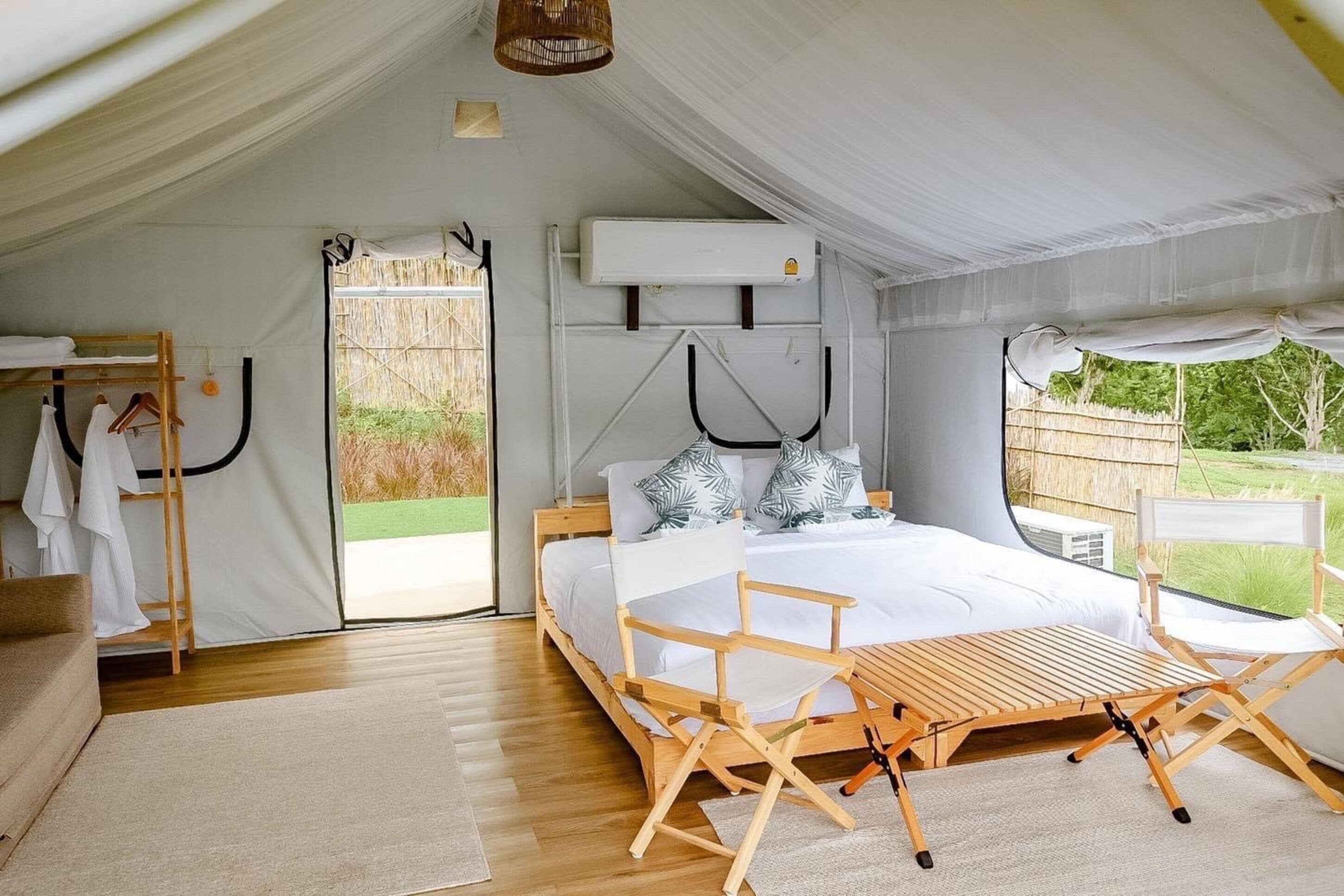 A tent-style bedroom with a bed, wooden chairs, a table, and an air conditioning unit.