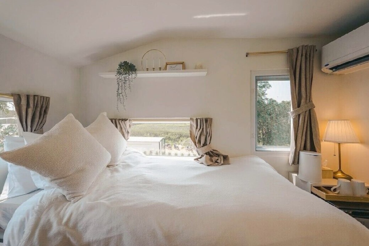 Une chambre d’hôtel avec un grand lit, une table de chevet avec une lampe, une fenêtre avec des rideaux et un appareil de climatisation.