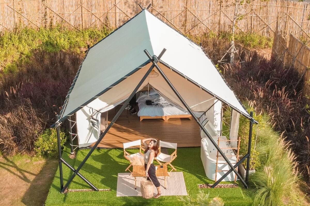 Une tente avec un lit à l’intérieur, entourée d’une zone herbeuse et d’une clôture en bambou.