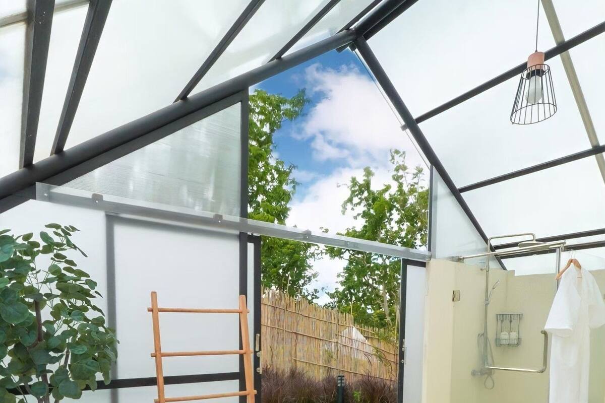 Une pièce entièrement vitrée comprenant un jacuzzi, une échelle, un panier en osier et un espace douche.