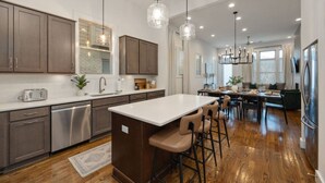 A modern kitchen with a central island, bar stools, and a dining area with a view of the living room. - West End- Best for Families, Work & College Visits (Nashville)