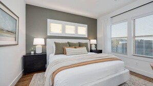 A bedroom with a large bed, two bedside tables with lamps, a headboard with three windows, and a view of the outside through the windows. - West End- Best for Families, Work & College Visits (Nashville)