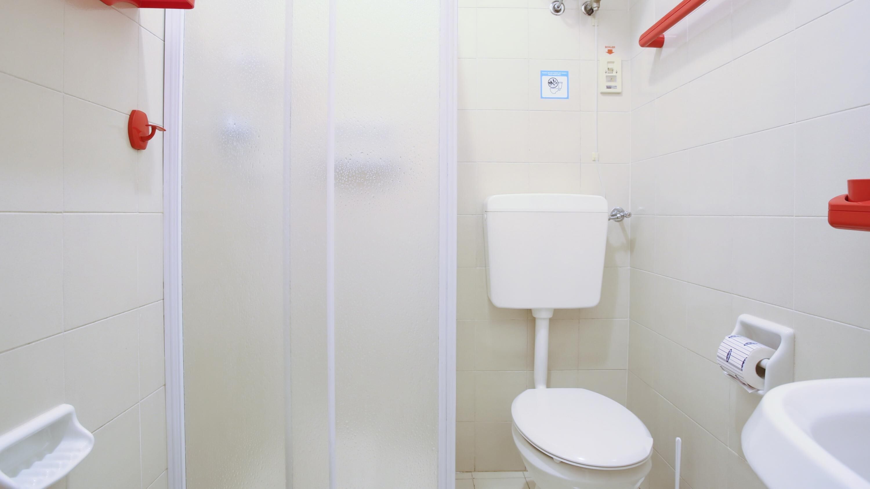 A small, clean bathroom with white tiles, a toilet, a shower, and a sink.