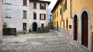 A cobblestone courtyard with buildings featuring arched doorways and traditional shutters.