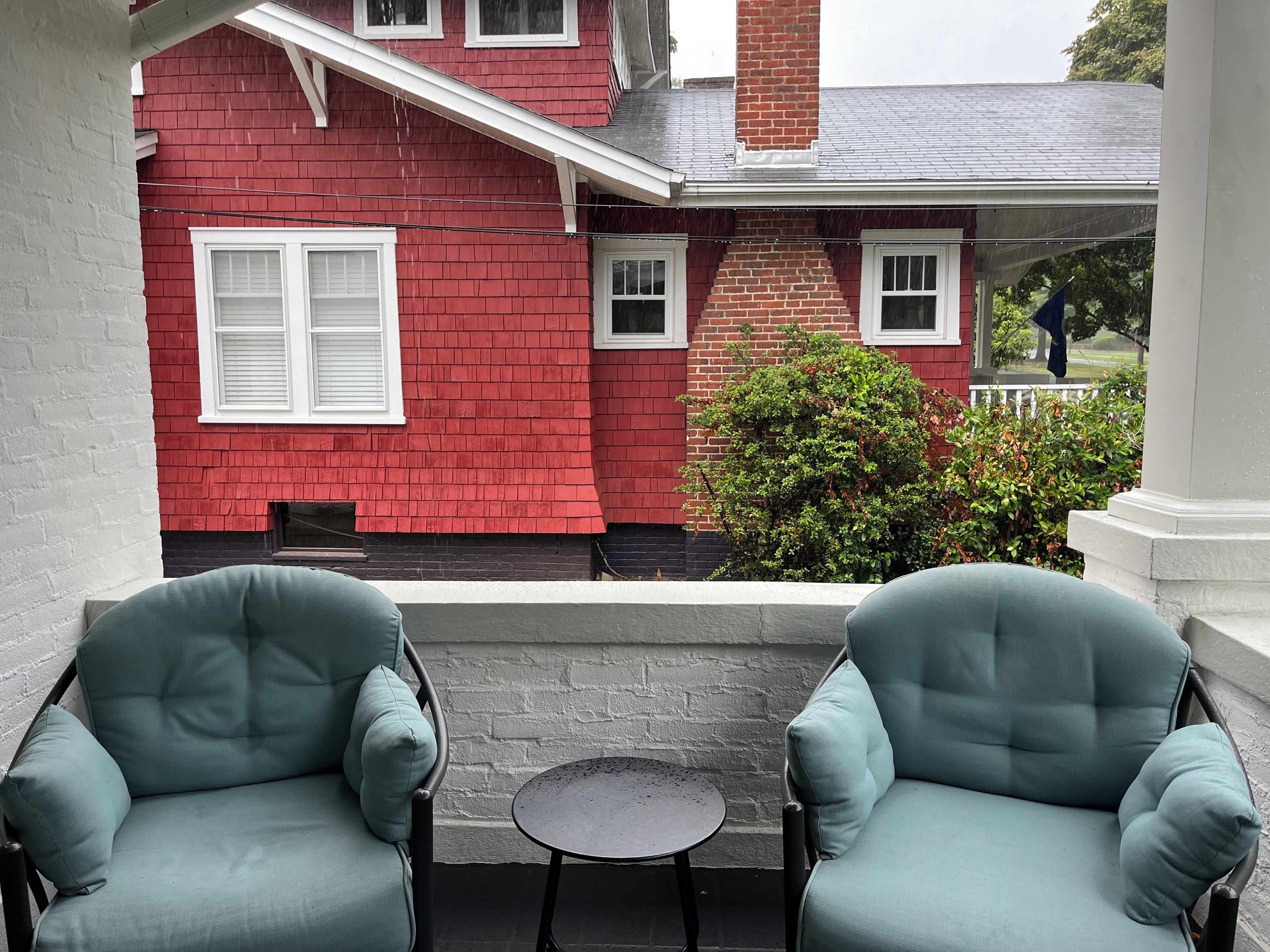 A red brick house with white shutters, a porch with a small table, and two light blue chairs.