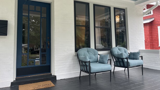 A porch with two light blue cushioned chairs, a black door, and large windows.