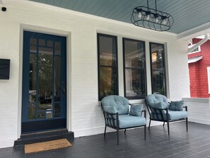 Une véranda avec deux fauteuils bleu clair dotés de coussins, une porte noire et de grandes fenêtres.