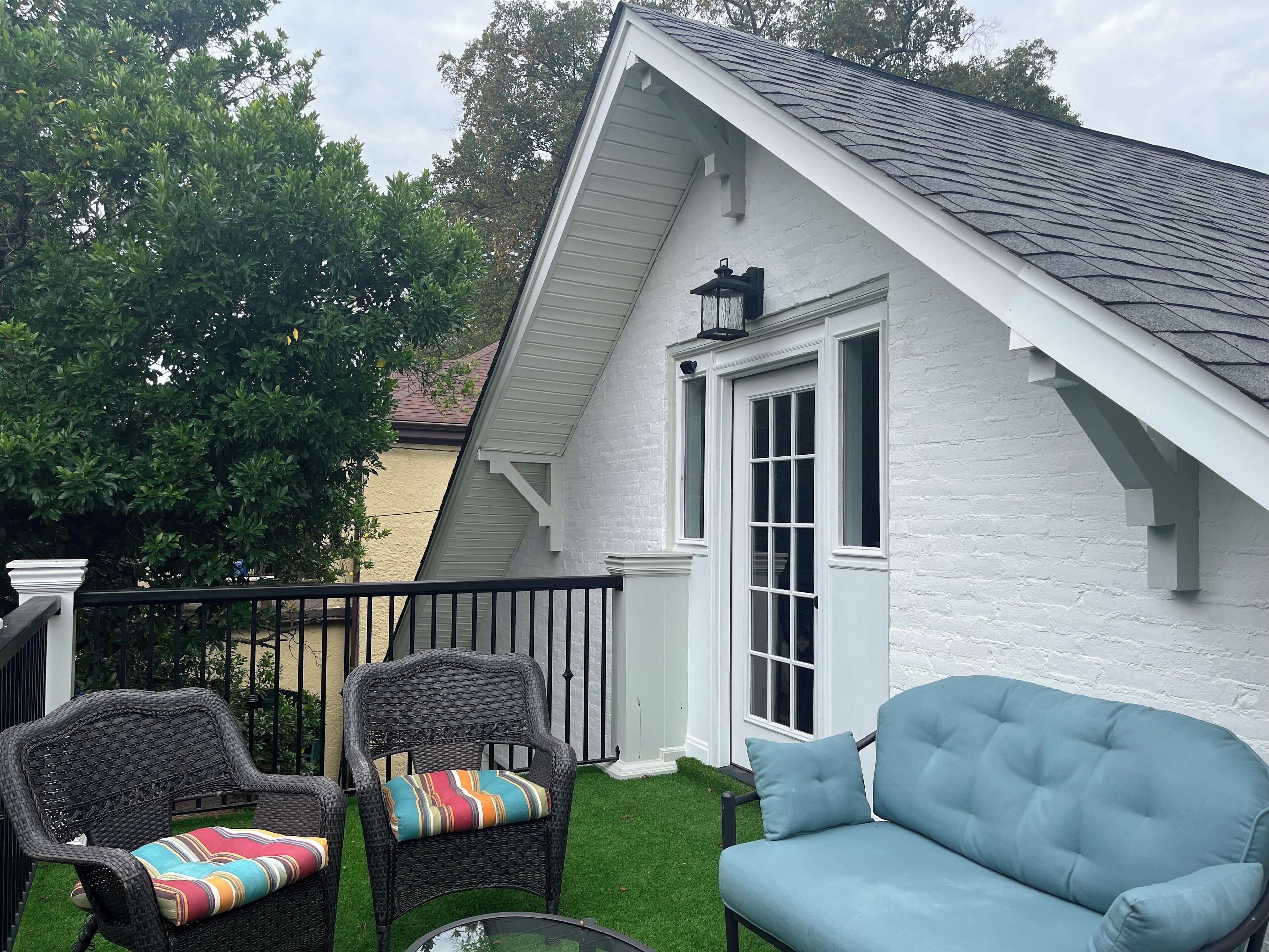 A white house with a black roof, a porch with wicker chairs, and a blue sofa.