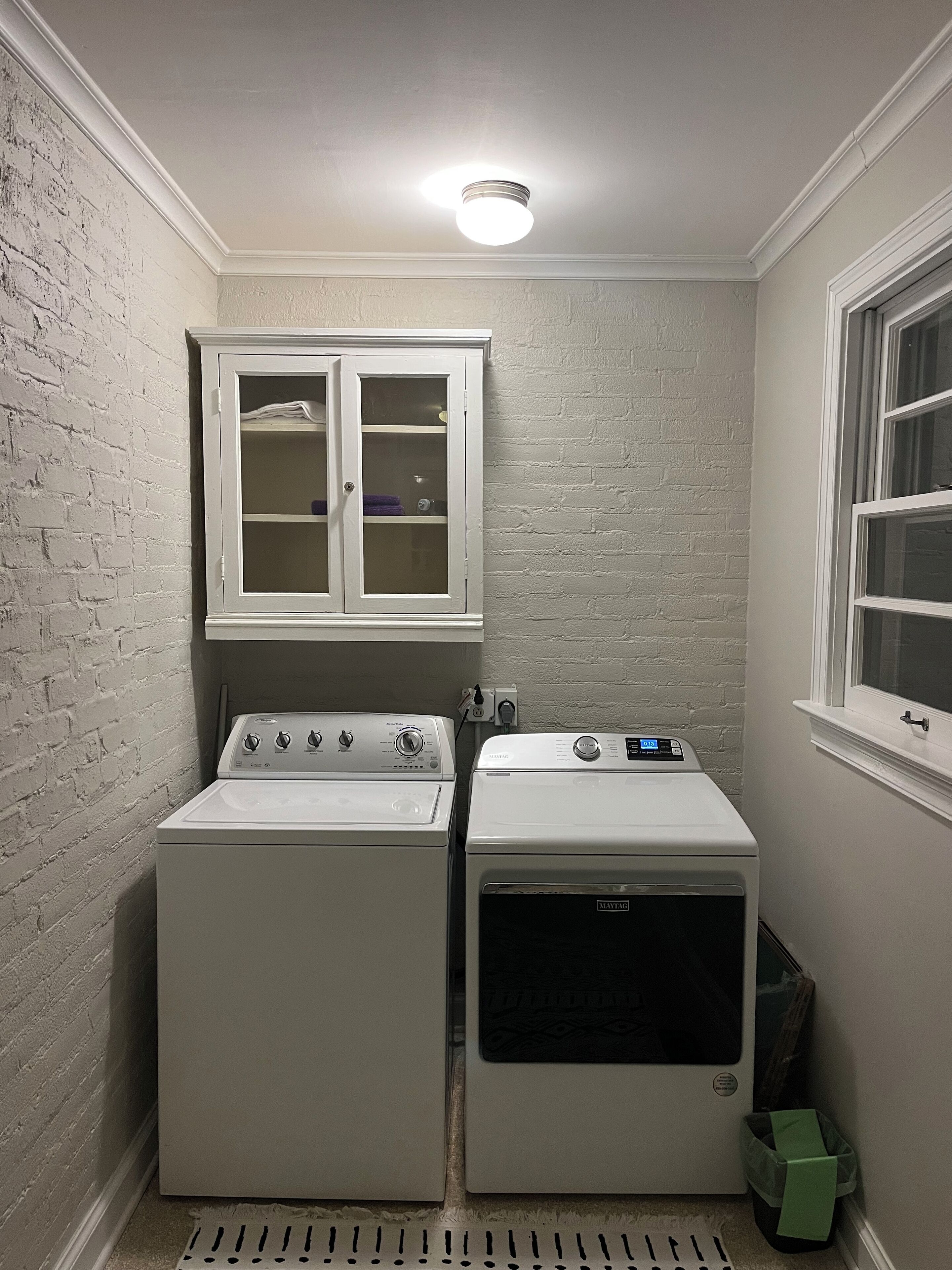 A laundry room with two washing machines, a cabinet, and a window.
