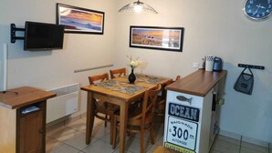 A dining area with a wooden table, chairs, a vase with flowers, a clock, and a sign indicating the property is 300 meters from the sea.