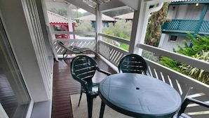 A covered outdoor area with a round table and four chairs, a wooden floor, and a white railing.
