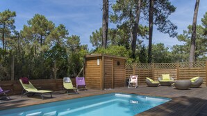 Eine Holzterrasse mit Schwimmbecken, umgeben von hohen Kiefern.