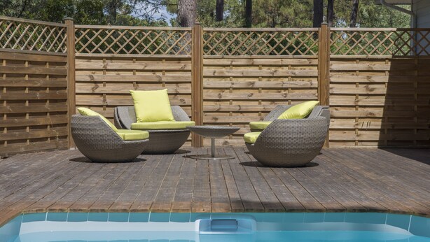 Ein Poolbereich mit Whirlpool, zwei Korbstühlen mit Kissen und einer Holzterrasse.
